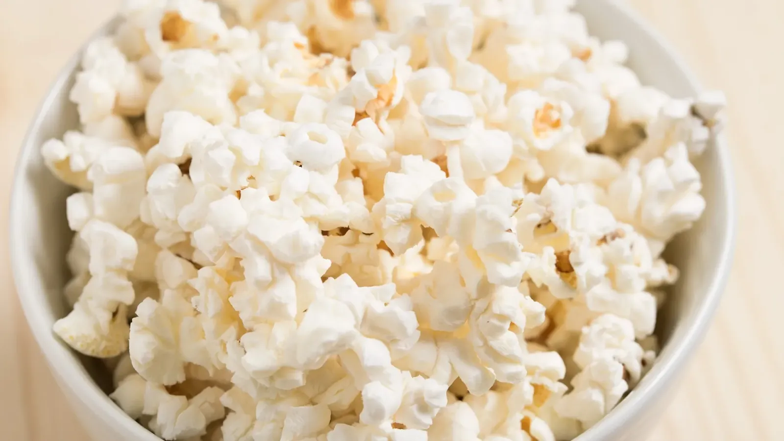Weiße Schale mit schlichtem, ungewürztem Popcorn auf einem hellen Holztisch