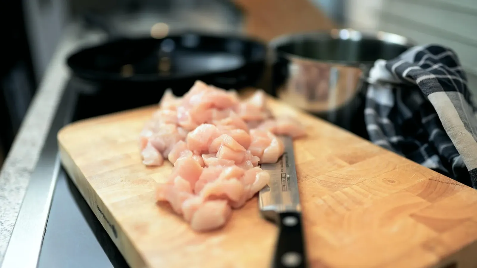 Gewürfeltes rohes Hähnchenfleisch auf einem Holzbrett mit Küchenmesser – Symbolbild zum Fleischanteil im Hunde- und Katzenfutter
