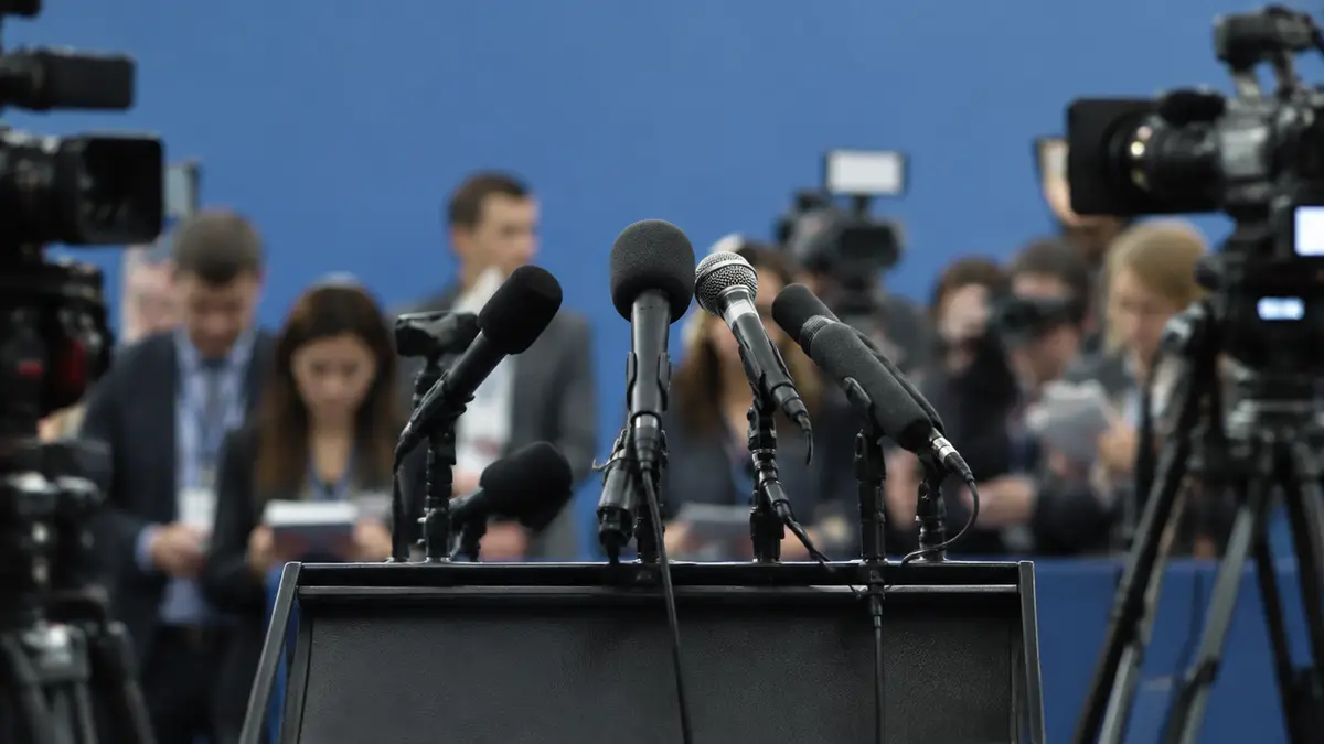 Pressekonferenz mit Mikrofonen und Kameras im Vordergrund